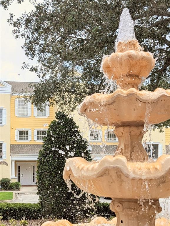 A tiered stone fountain stands in front of a yellow multi-story building with white trim — 1338 SEVEN EAGLES COURT UNIT 202, REUNION, FL