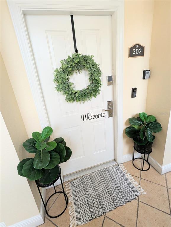 A white front door with a wreath and welcome sign is flanked by two potted plants — 1338 SEVEN EAGLES COURT UNIT 202, REUNION, FL