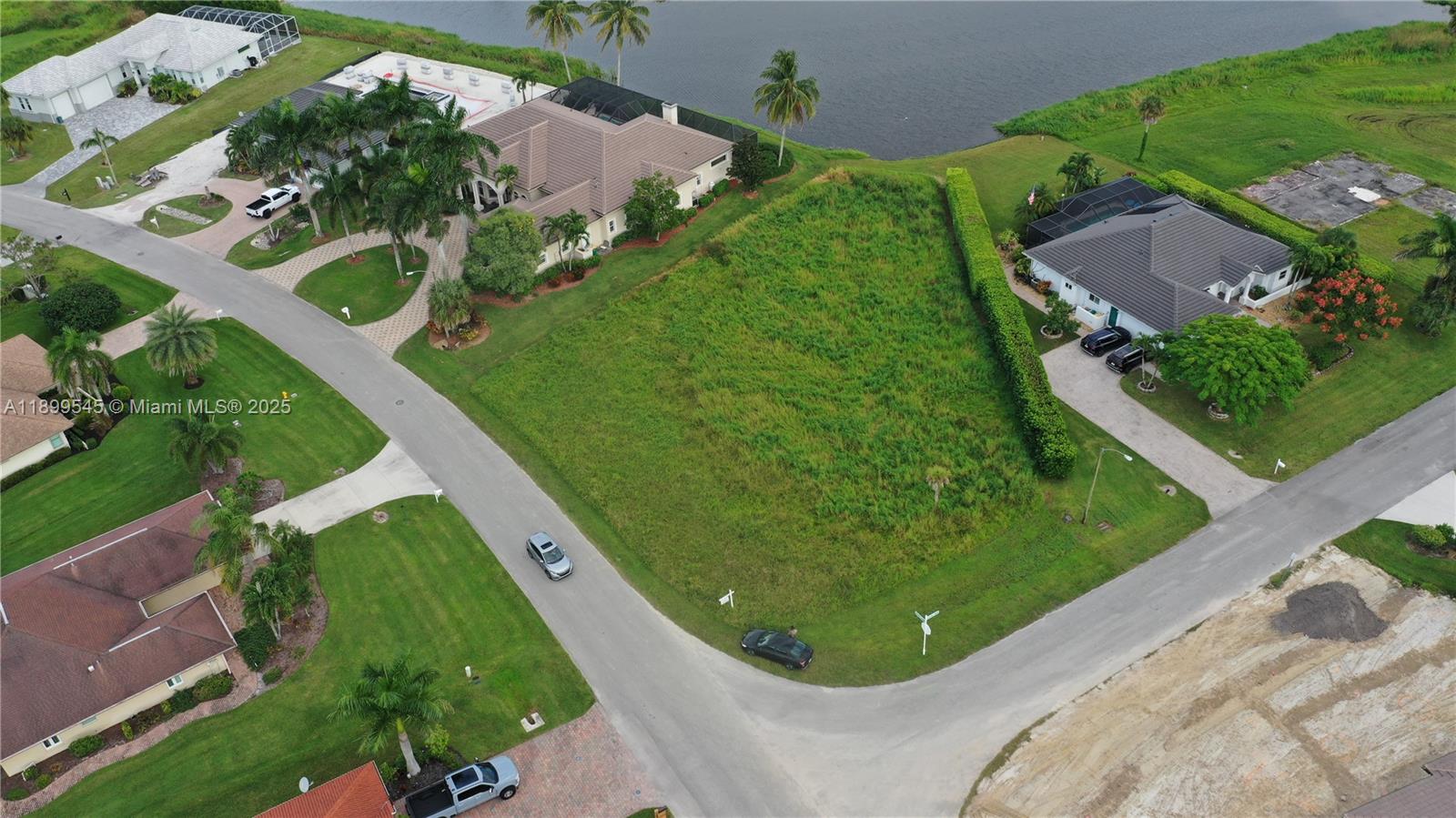 An aerial view shows a vacant, grassy residential lot situated between two houses and water — 18018 Royal Hammock Blvd, Naples FL 34114, NAPLES, FL