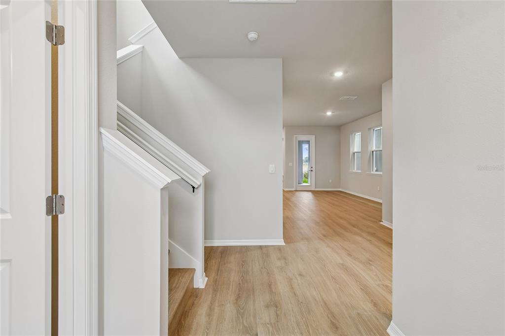 A hallway features wood-look flooring, a console table with a lamp, and abstract wall art — 9334 HARTLINE WAY, ORLANDO, FL