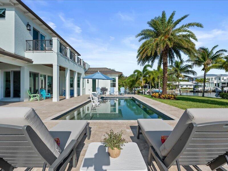 A patio with lounge chairs overlooks a swimming pool and a canal with palm trees — 205 Body Court, Jupiter FL 33477, JUPITER, FL