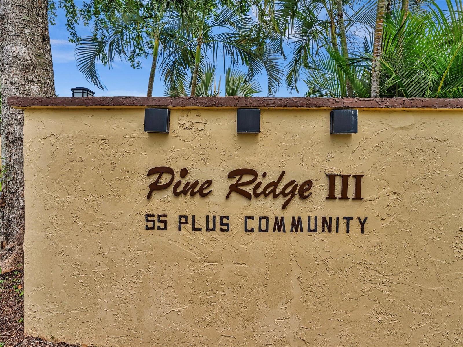 A beige stucco wall displays the text Pine Ridge III 55 Plus Community — 342 Pine Ridge Circle # 2, FL 33463, FL