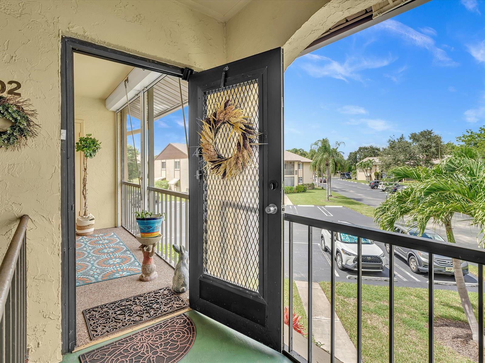 A screened-in balcony features a decorative door, outdoor rugs, potted plants, and a parking lot view — 342 Pine Ridge Circle # 2, FL 33463, FL