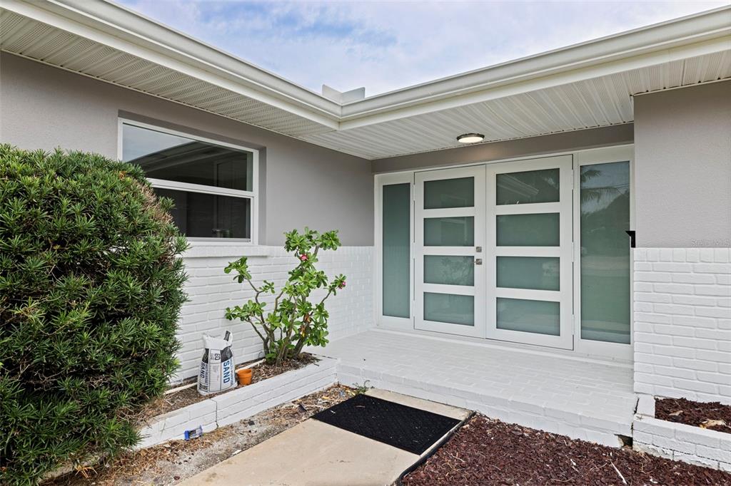 The exterior of a house features a white brick facade, double glass doors, and landscaping — 7073 S SHORE DRIVE S, ST PETERSBURG, FL