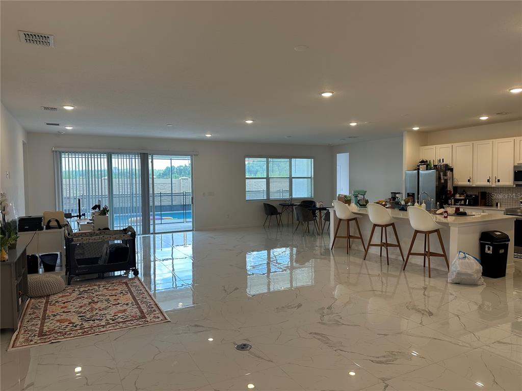 An open-concept living area features white marble-look tile floors, a kitchen island, and sliding glass doors — 3800 SONOMA BOULEVARD, KISSIMMEE, FL