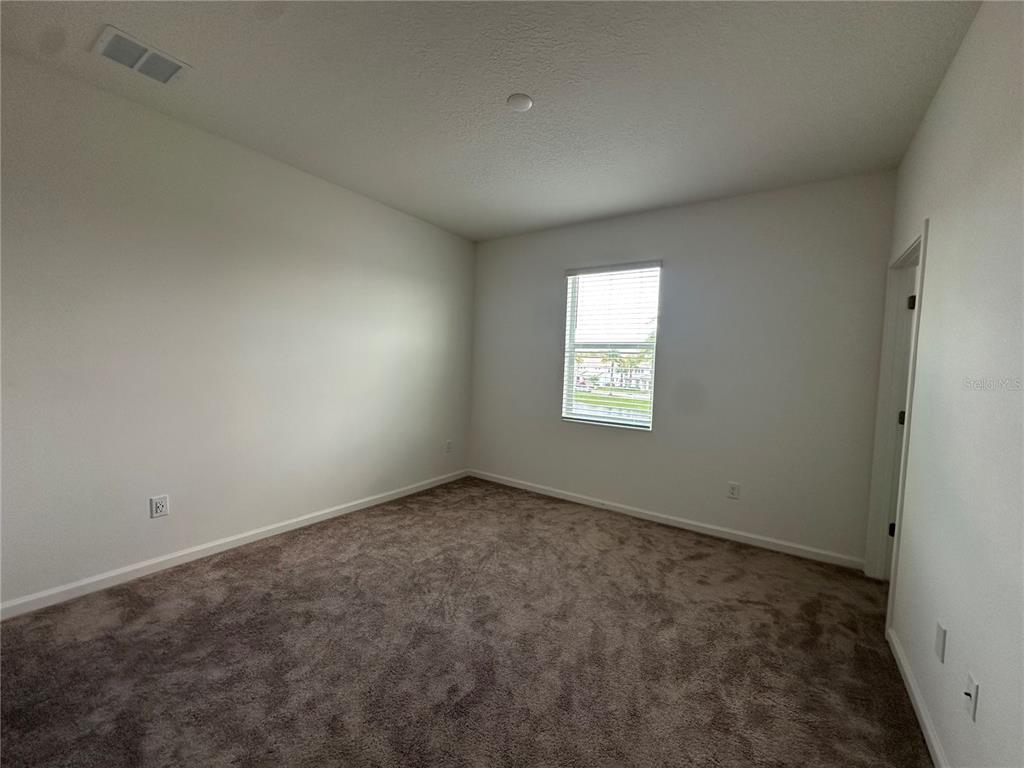 An empty bedroom features neutral walls, brown carpeting, and a single window with blinds — 3800 SONOMA BOULEVARD, KISSIMMEE, FL