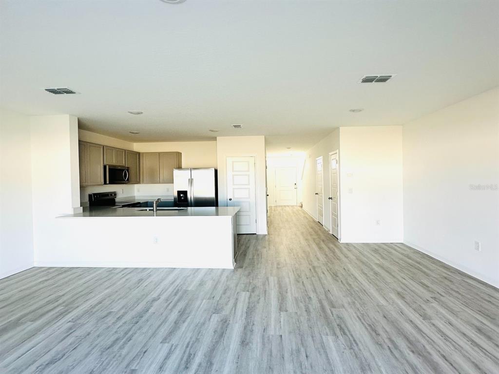 An open-concept kitchen with stainless steel appliances overlooks a living area with wood-look flooring — 1335 TALLOWWOOD LANE, DAVENPORT, FL