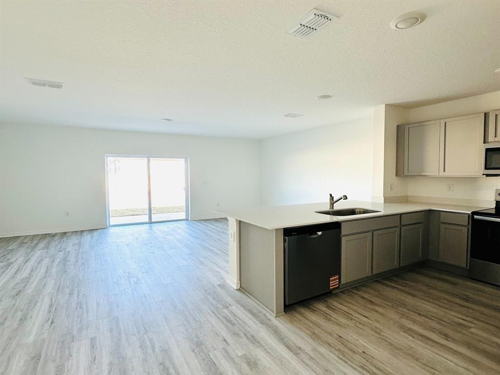 An open-concept kitchen with gray cabinets and a breakfast bar overlooks a living area — 1335 TALLOWWOOD LANE, DAVENPORT, FL