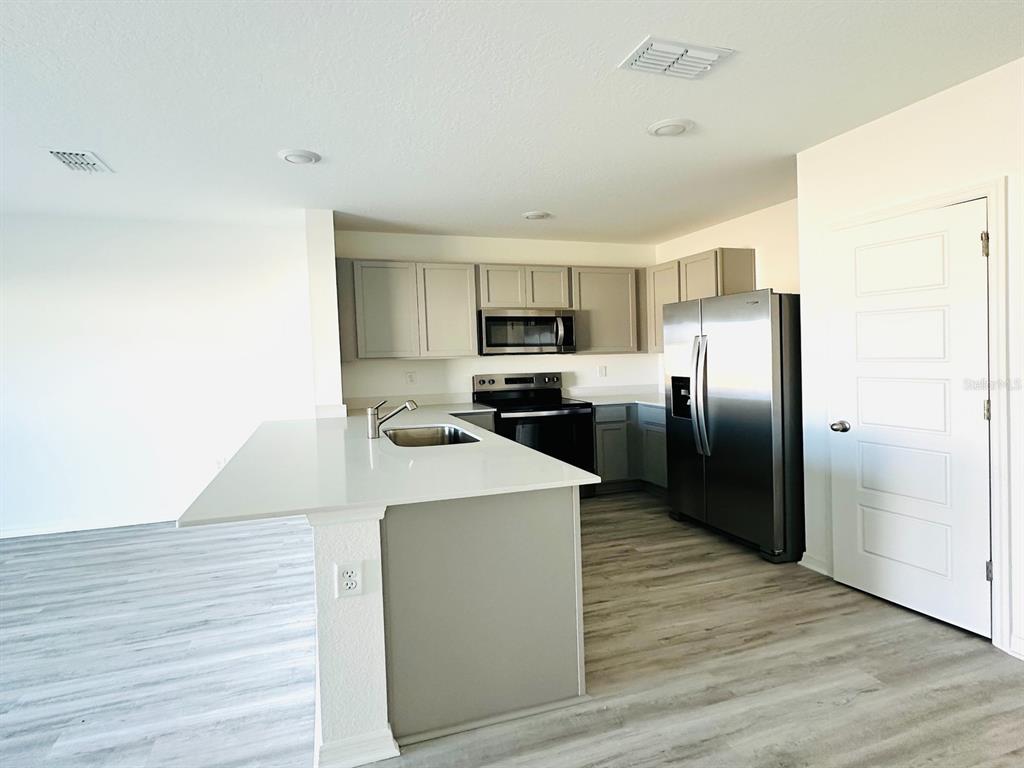 A kitchen features light gray cabinets, stainless steel appliances, and a white quartz island countertop — 1335 TALLOWWOOD LANE, DAVENPORT, FL