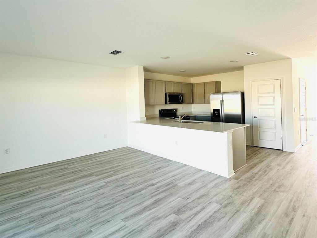 An open-concept kitchen with light gray cabinets and stainless steel appliances overlooks a living area — 1335 TALLOWWOOD LANE, DAVENPORT, FL