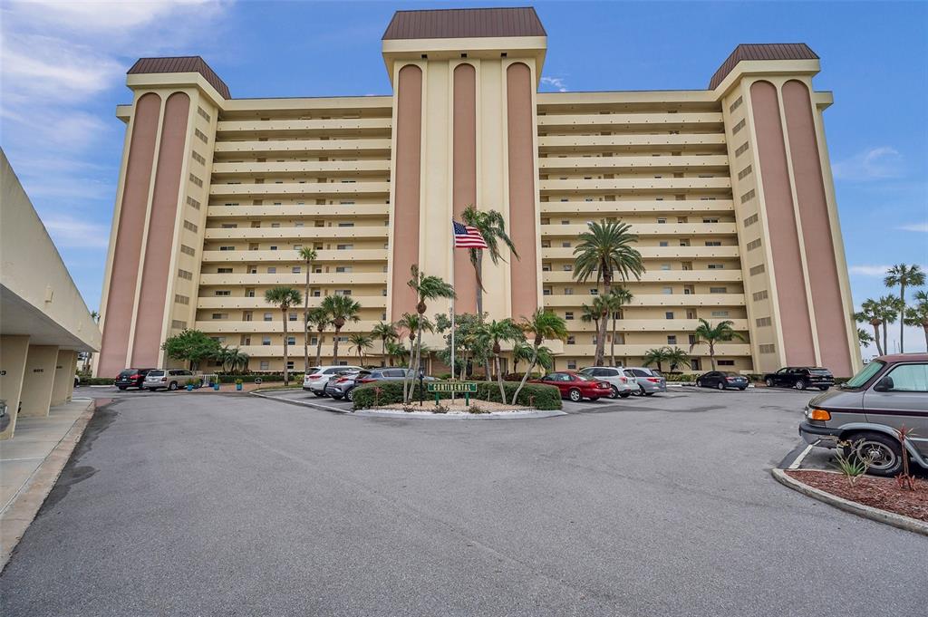 A multi-story beige apartment building with a parking lot and palm trees in front — 4775 COVE CIRCLE N UNIT 104, ST PETERSBURG, FL
