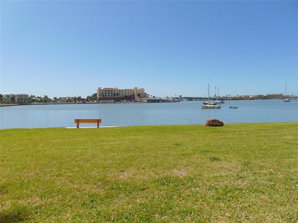 A grassy waterfront park features a wooden bench and a view of boats and buildings — 4775 COVE CIRCLE N UNIT 104, ST PETERSBURG, FL