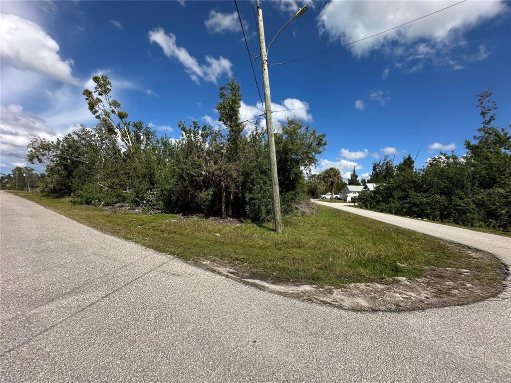 A paved road curves around a vacant, tree-covered corner lot with a utility pole — 4315 GARDEN ROAD, PORT CHARLOTTE, FL