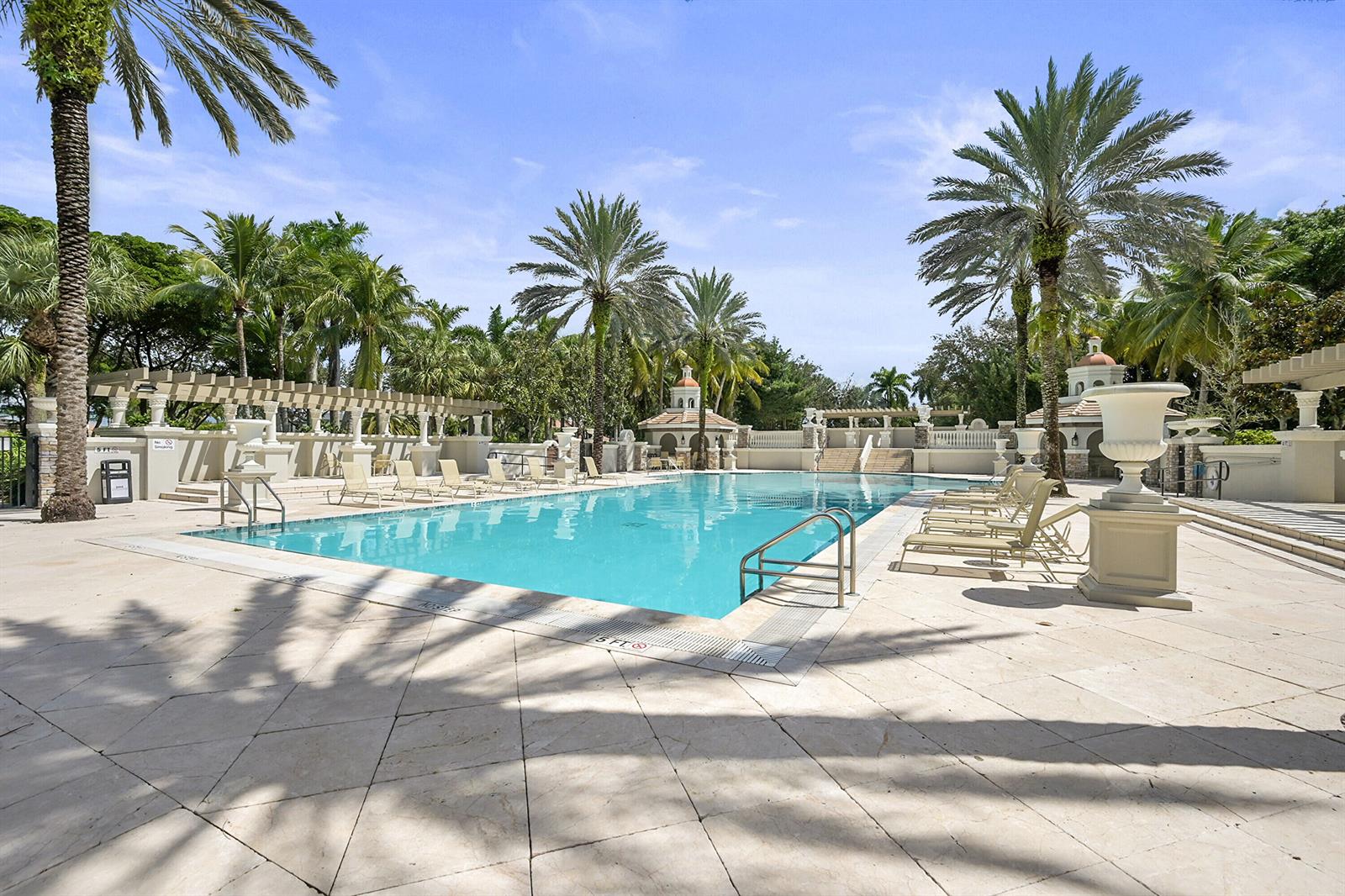 A rectangular swimming pool is surrounded by a stone patio, lounge chairs, and palm trees — 10340 Trianon Place, Wellington FL 33449, WELLINGTON, FL