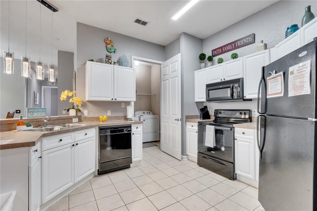 A kitchen with white cabinets, black appliances, tile flooring, and a laundry room doorway — 505 TERRACE RIDGE CIRCLE UNIT 505, DAVENPORT, FL