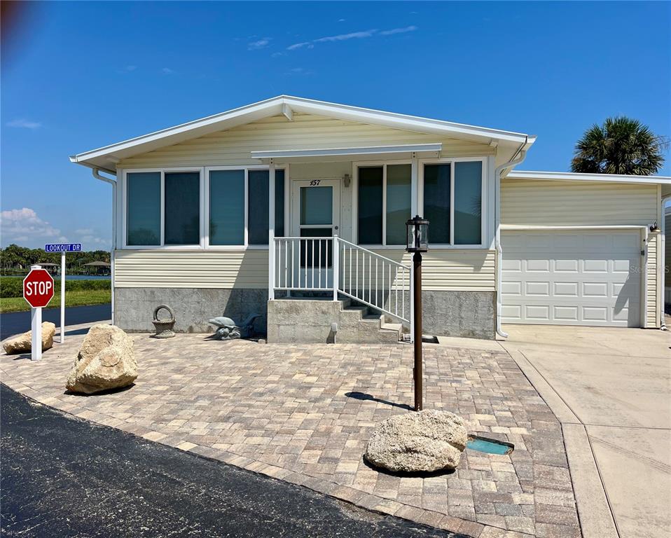 A light-colored manufactured home features a paved front patio, a garage, and a stop sign — 157 LOOKOUT DRIVE, FLAGLER BEACH, FL