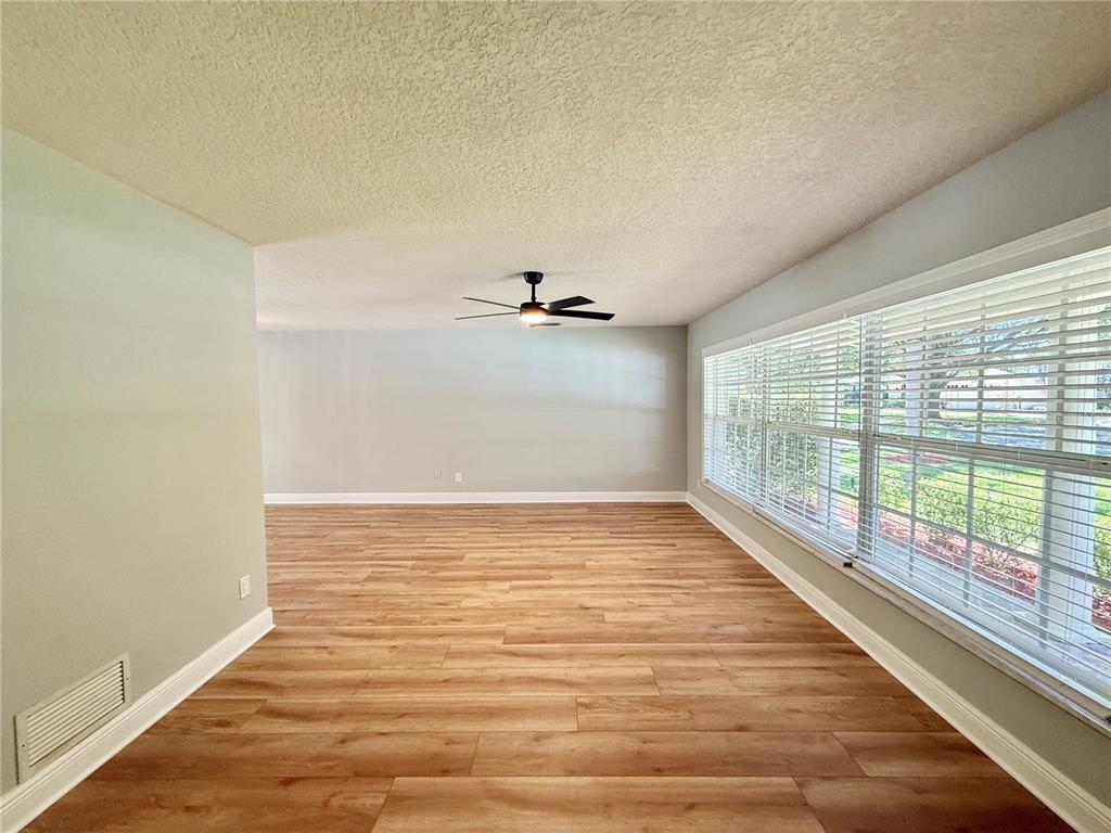 An empty room with light wood-look flooring, a ceiling fan, and large windows with blinds — 1625 TIOGA TRAIL, WINTER PARK, FL