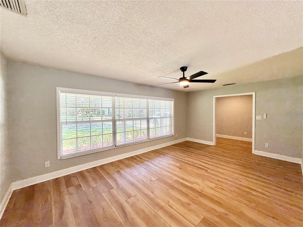 A living room with light gray walls, wood-look flooring, a ceiling fan, and large windows — 1625 TIOGA TRAIL, WINTER PARK, FL