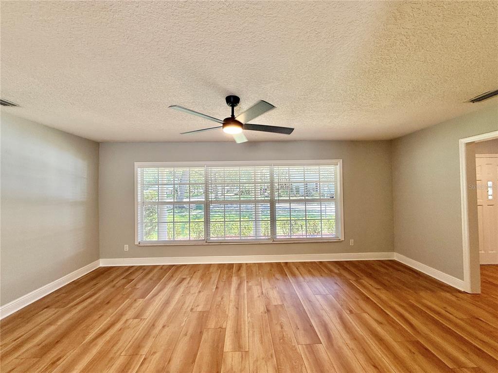 An empty room features light gray walls, wood-look flooring, a ceiling fan, and a large window — 1625 TIOGA TRAIL, WINTER PARK, FL