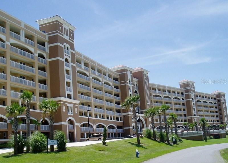 A multi-story tan apartment building with balconies stands above a grassy lawn and palm trees — 60 SURFVIEW DRIVE UNIT 122, PALM COAST, FL