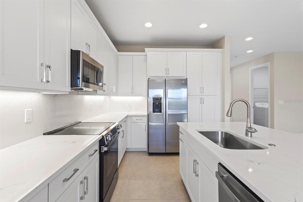 A modern kitchen features white cabinets, stainless steel appliances, and a large quartz-topped island — 14005 ALDERSGATE AVENUE, FORT MYERS, FL