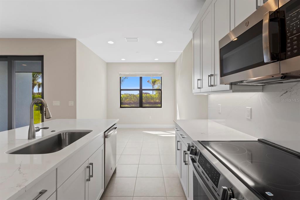 A modern kitchen with white cabinets, stainless steel appliances, and a central island with sink — 14005 ALDERSGATE AVENUE, FORT MYERS, FL