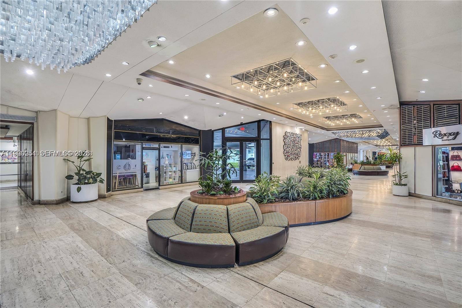 A bright, modern indoor lobby features a circular seating area, potted plants, and decorative lighting — 999 Brickell Bay Drive # 1202, Miami FL 33131, MIAMI, FL