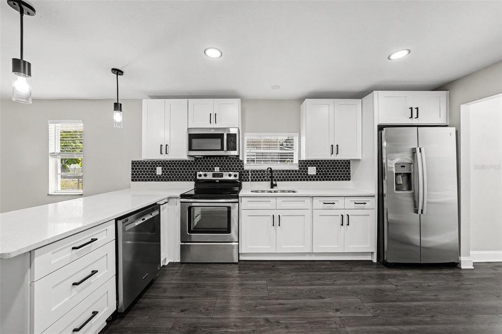 A modern kitchen features white cabinets, stainless steel appliances, and a black honeycomb tile backsplash — 1204 E CAYUGA STREET, TAMPA, FL