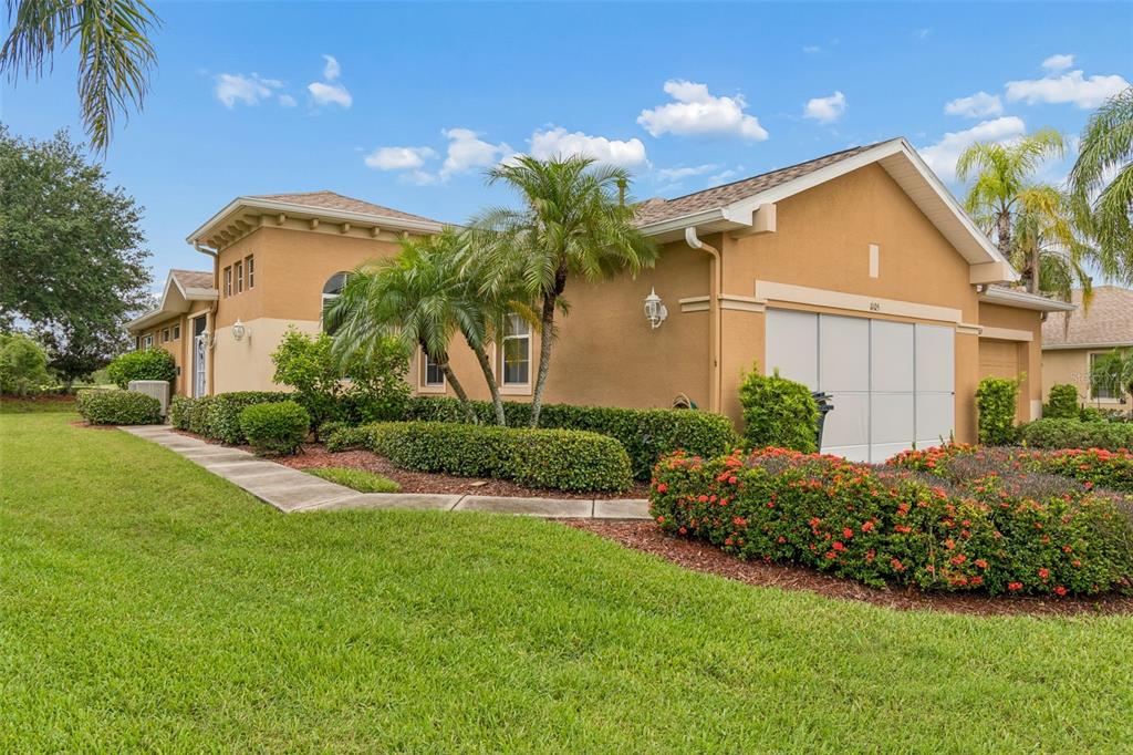 A tan stucco house with a two-car garage, palm trees, and landscaped bushes — 1105 JAMESON GREENS DRIVE UNIT 1105, SUN CITY CENTER, FL