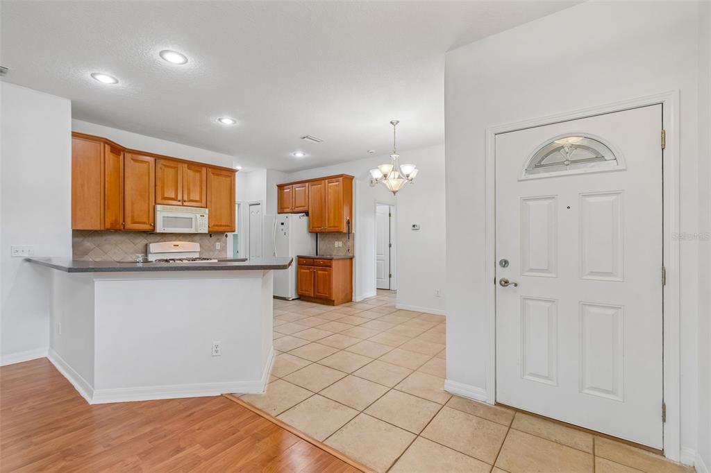 A kitchen with wood cabinets and a breakfast bar overlooks a tiled entryway and door — 1105 JAMESON GREENS DRIVE UNIT 1105, SUN CITY CENTER, FL