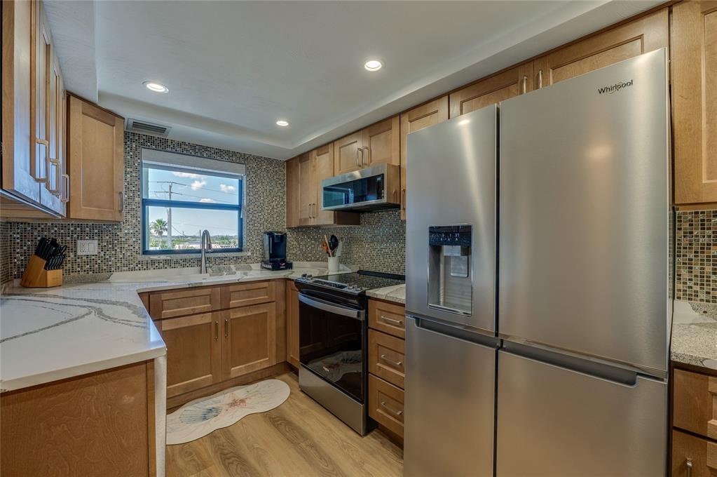 A kitchen with light wood cabinets, stainless steel appliances, and a mosaic tile backsplash — 3800 S ATLANTIC AVENUE UNIT 207, DAYTONA BEACH, FL