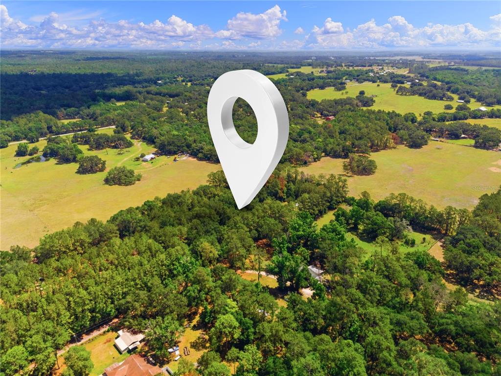 An aerial view shows a large white map pin hovering over a wooded rural landscape — 1074 CULBREATH ROAD, BROOKSVILLE, FL
