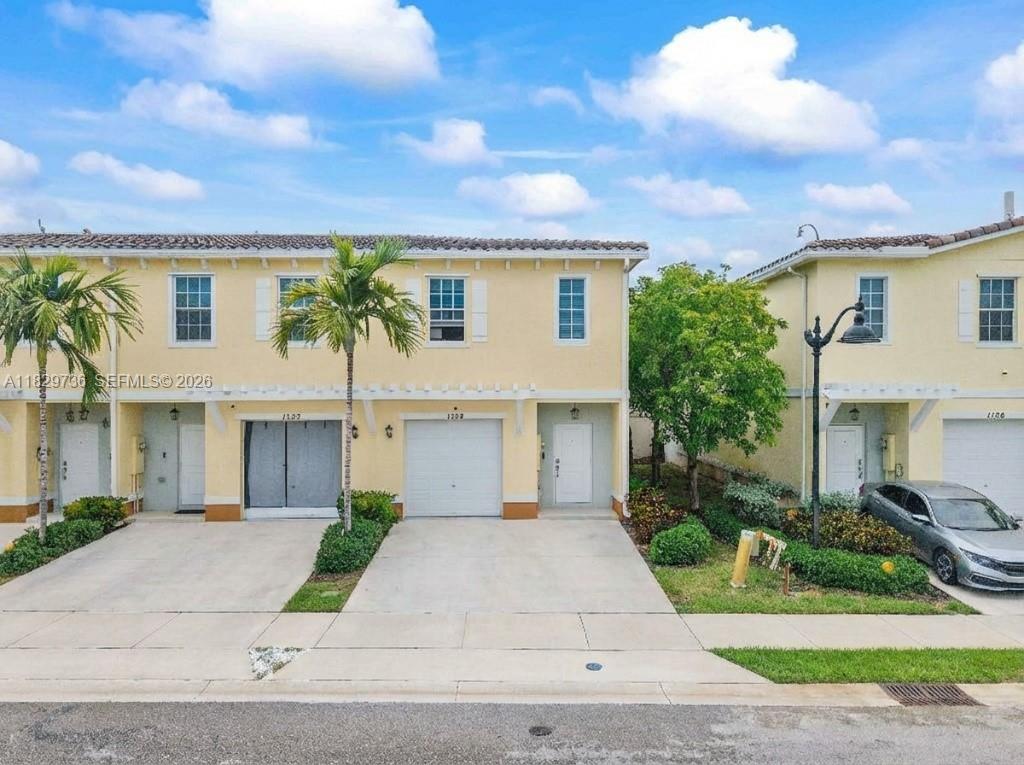 A two-story townhouse with a light yellow exterior, a garage, and a concrete driveway — 1128 NW 40th Ter, Lauderhill FL 33313, LAUDERHILL, FL