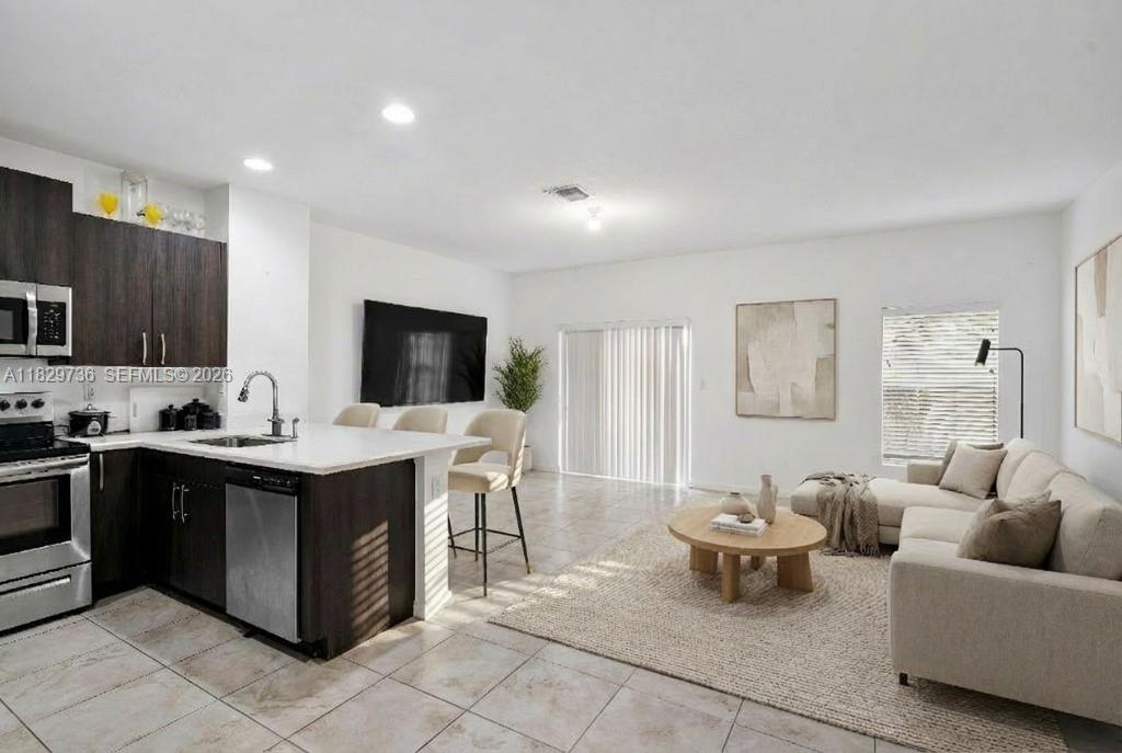 A modern open-concept kitchen and living area features dark wood cabinetry and neutral furniture — 1128 NW 40th Ter, Lauderhill FL 33313, LAUDERHILL, FL
