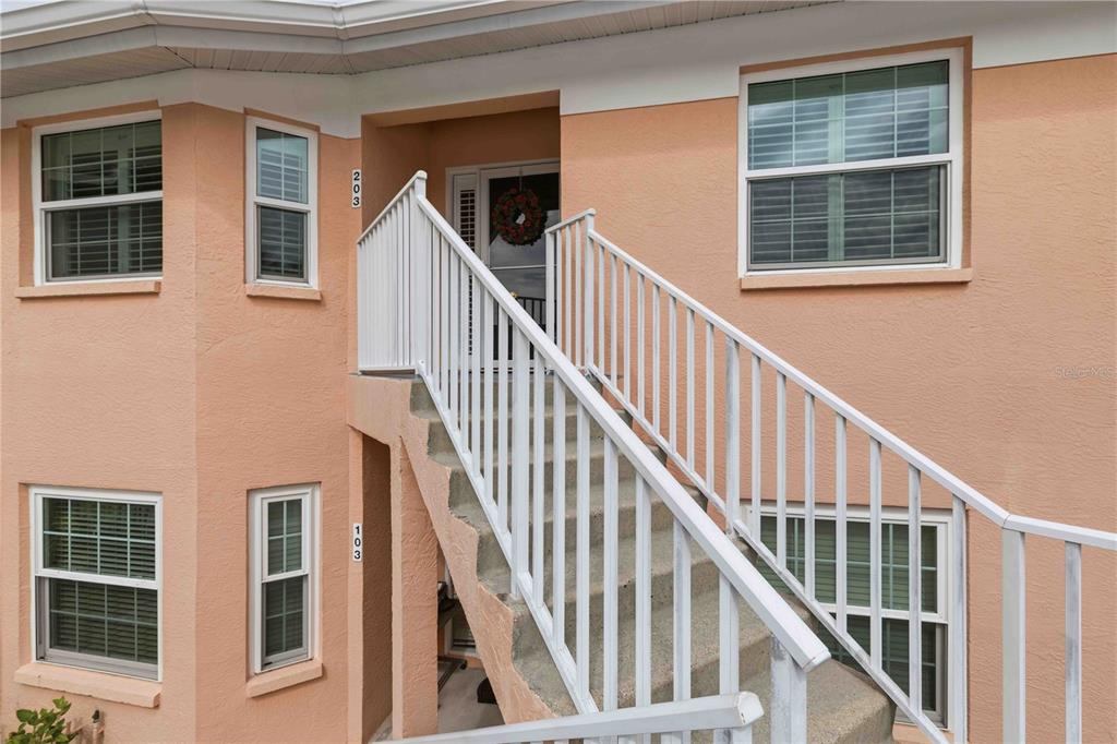 An exterior view of a peach-colored building featuring a staircase leading to an upper entrance — 19310 WATER OAK DRIVE UNIT 203, PORT CHARLOTTE, FL