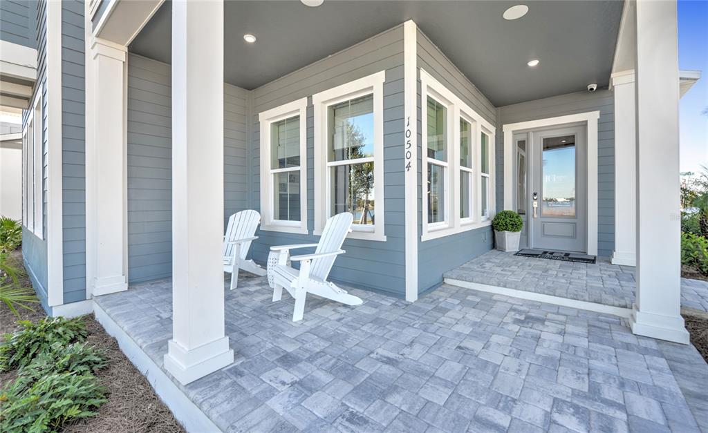 A covered front porch features gray siding, white columns, two white chairs, and paver flooring — 10504 PEARSON AVENUE, ORLANDO, FL