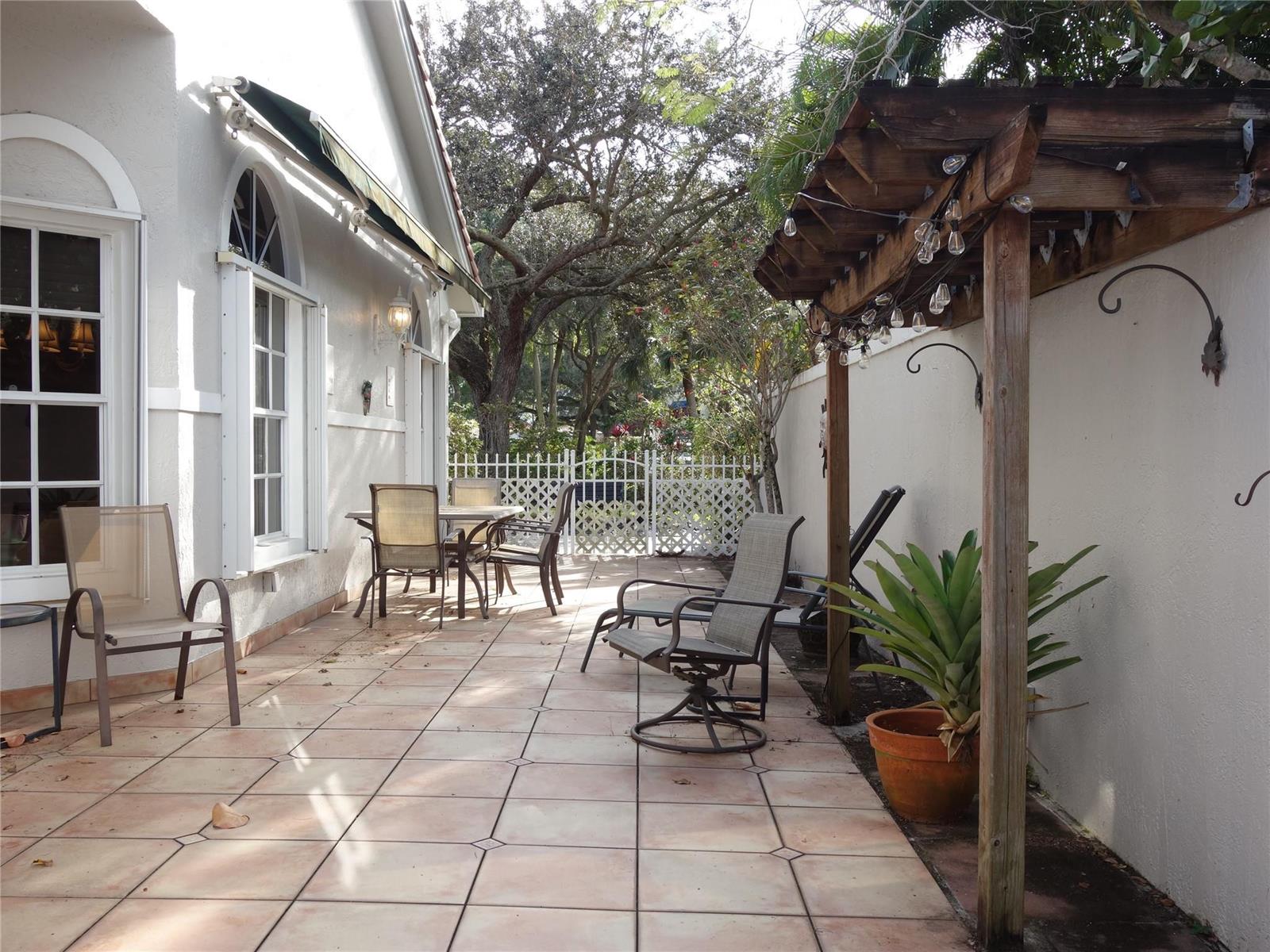 A paved patio features outdoor furniture, a wooden pergola with string lights, and a white fence — 4106 Carriage Drive # 5C, Pompano Beach FL 33069, POMPANO BEACH, FL