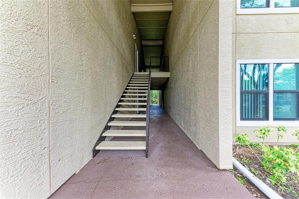 An exterior staircase leads to an upper-level walkway between two beige stucco apartment building walls — 4040 CROCKERS LAKE BOULEVARD UNIT 12, SARASOTA, FL