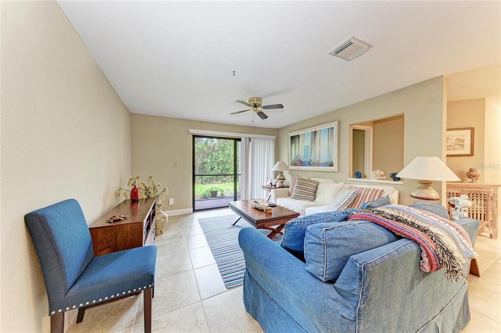 A living room features tile floors, a blue sofa, a blue chair, and a sliding door — 4040 CROCKERS LAKE BOULEVARD UNIT 12, SARASOTA, FL