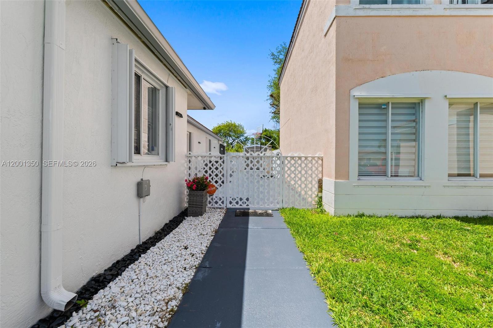 A paved walkway leads to a white lattice gate between two residential buildings — 17434 SW 143rd Pl, Miami FL 33177, MIAMI, FL