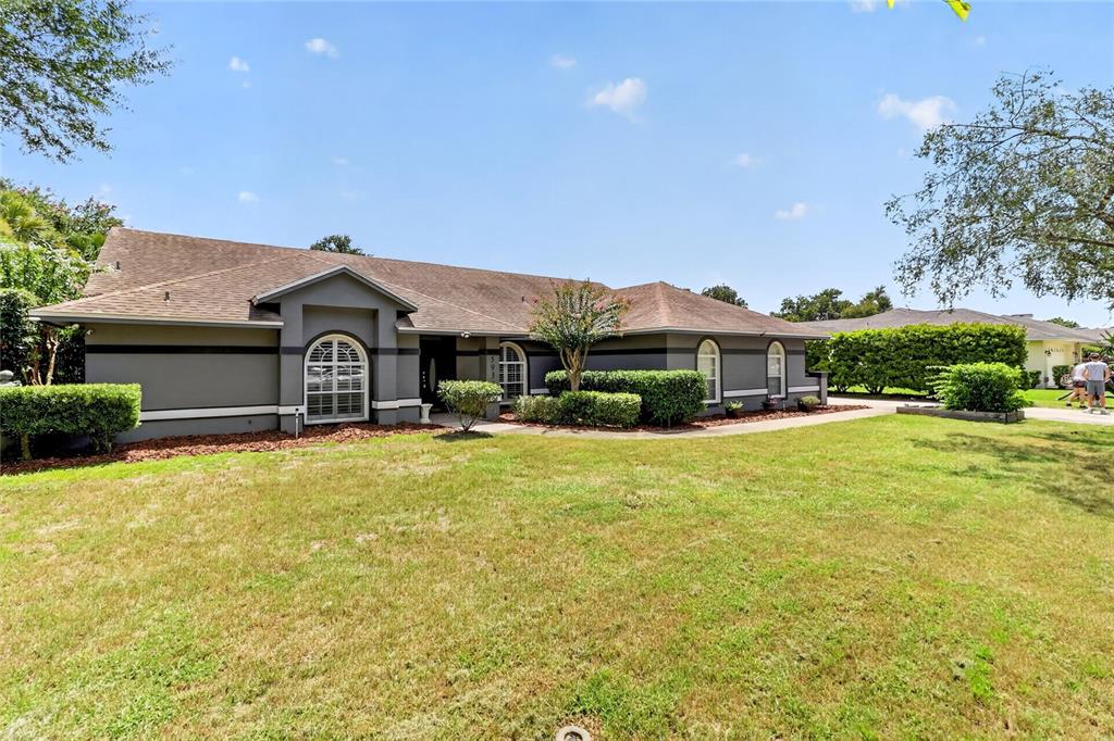 A single-story gray house with a brown shingled roof and arched windows sits on grass — 5939 WINDWOOD DRIVE, LAKELAND, FL