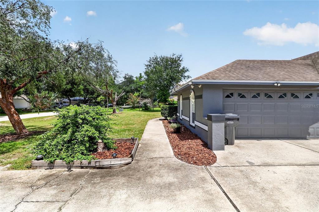 A concrete walkway leads past a landscaped garden bed toward the side of a house — 5939 WINDWOOD DRIVE, LAKELAND, FL