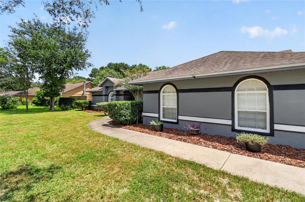 A gray house exterior features arched windows, a concrete walkway, and a landscaped yard — 5939 WINDWOOD DRIVE, LAKELAND, FL