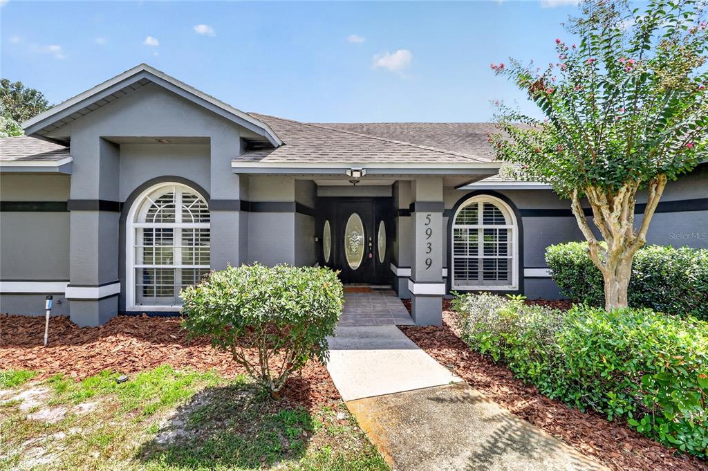 The exterior of a gray house features a covered entryway, arched windows, and landscaping — 5939 WINDWOOD DRIVE, LAKELAND, FL