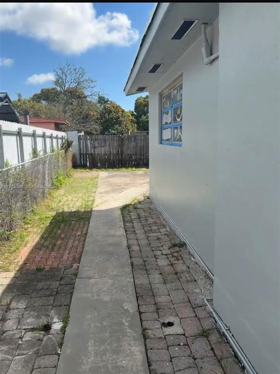 A narrow concrete walkway runs alongside the exterior wall of a house with brick pavers — 1637 NW 31st Ave, Miami FL 33125, MIAMI, FL