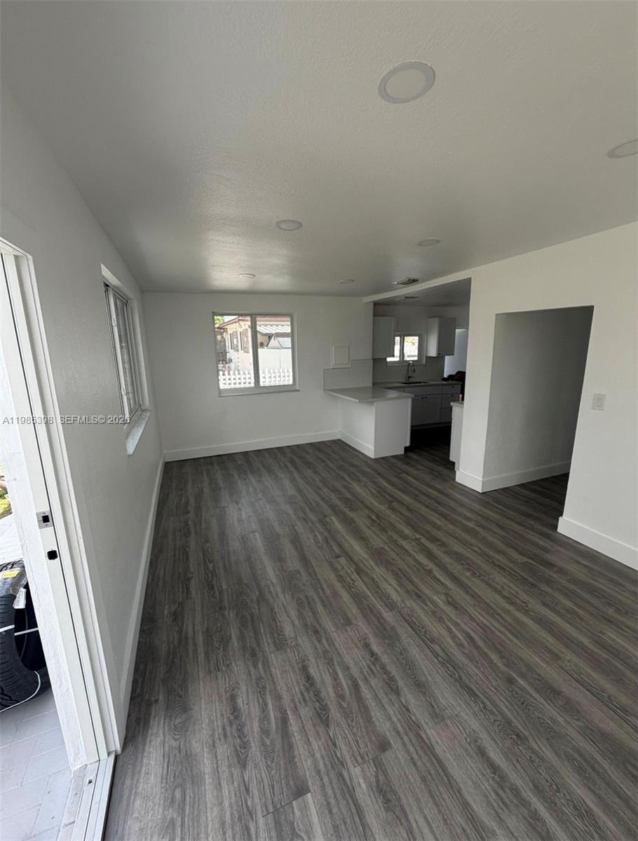 An empty room features gray wood-look flooring, white walls, recessed lighting, and an adjacent kitchen — 1637 NW 31st Ave, Miami FL 33125, MIAMI, FL
