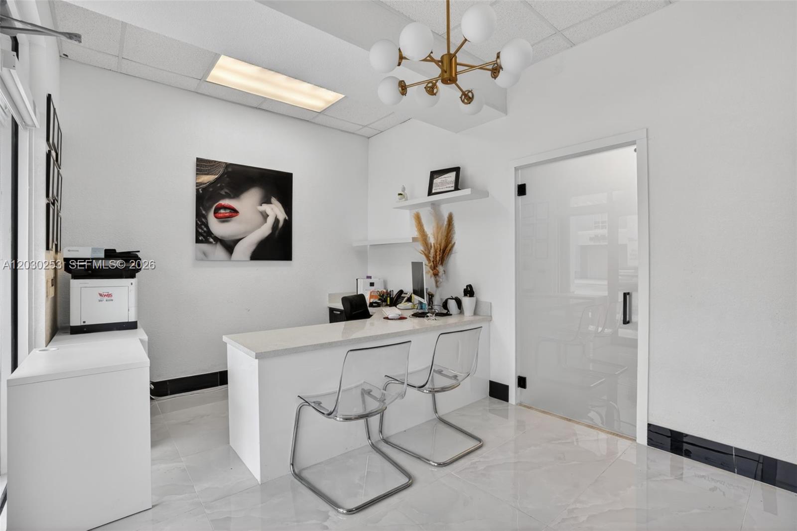 A modern office space features a white desk, two clear chairs, and a gold chandelier — 17690 NW 78th Ave, Hialeah FL 33015, HIALEAH, FL
