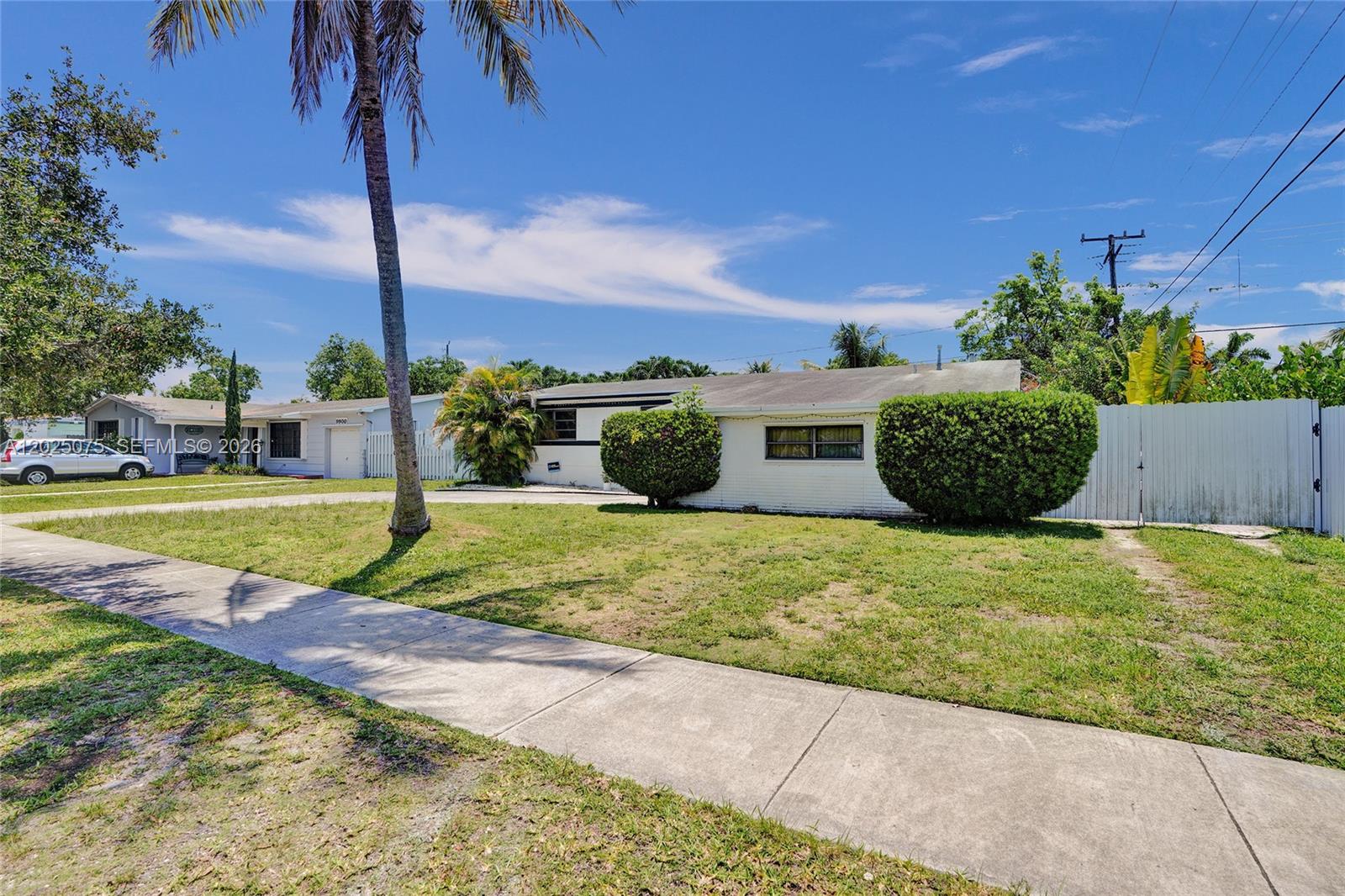 A single-story white house with a lawn, palm tree, and privacy fence under a blue sky — 9910 Bahama Dr, Cutler Bay FL 33189, CUTLER BAY, FL