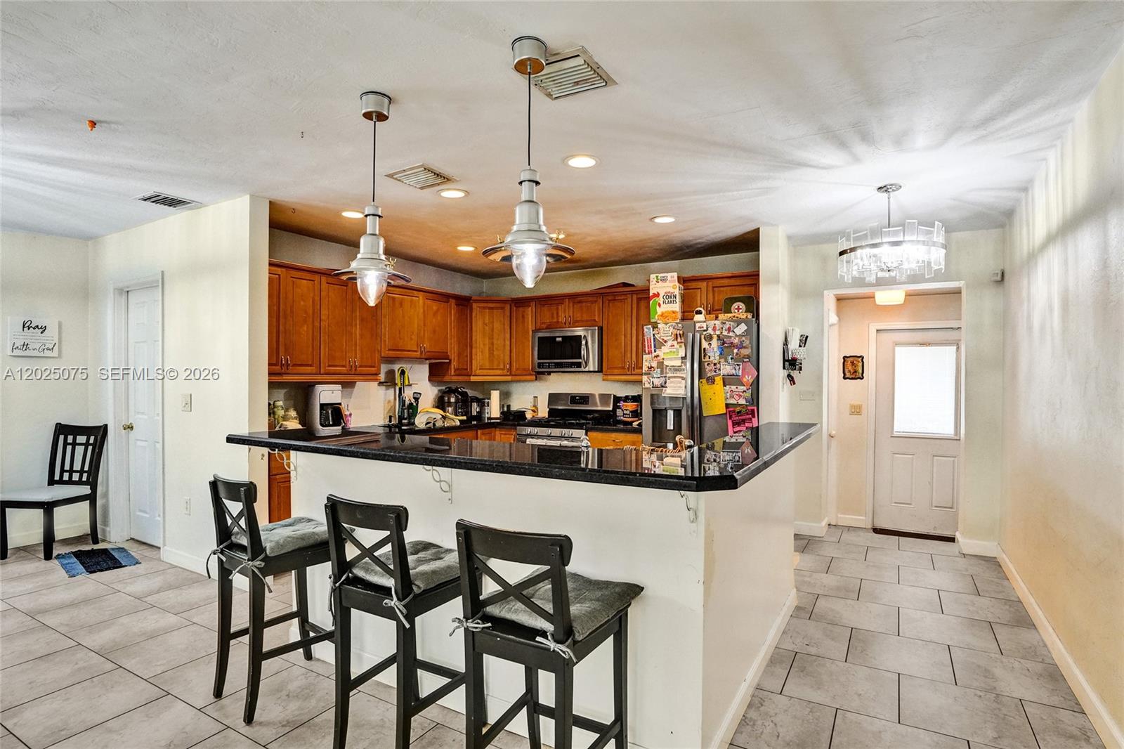 A kitchen features wood cabinets, black countertops, a breakfast bar with stools, and tile flooring — 9910 Bahama Dr, Cutler Bay FL 33189, CUTLER BAY, FL