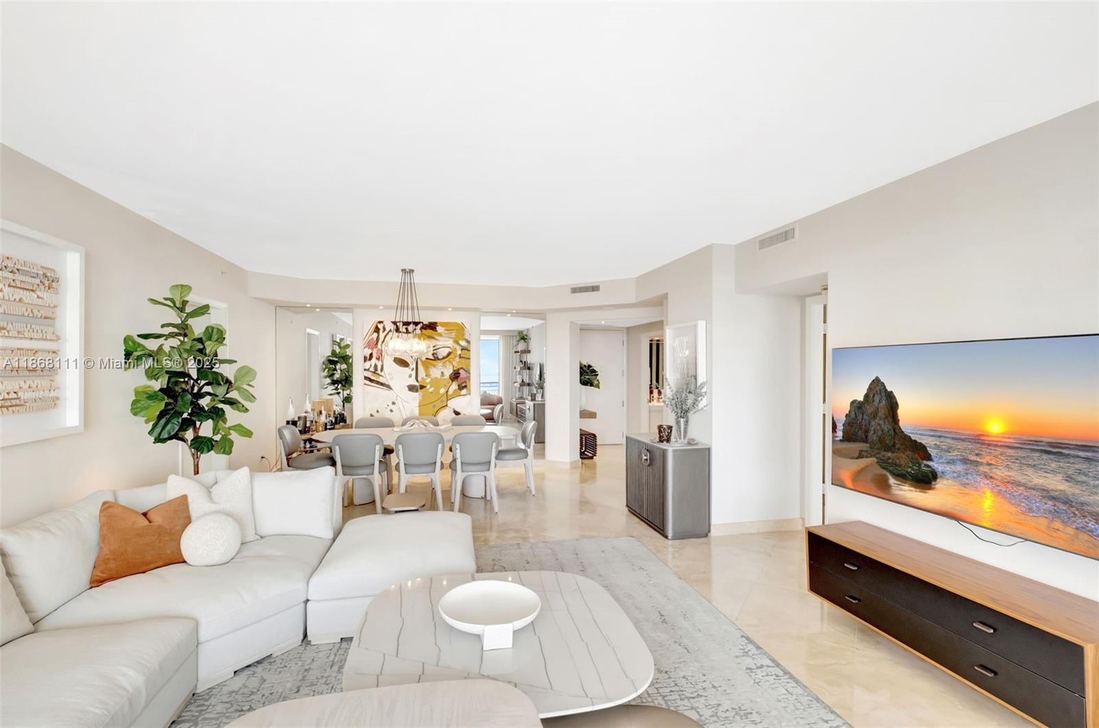 A bright living and dining area features a white sectional sofa, marble floors, and television — 848 Brickell Key Dr # 2605, Miami FL 33131, MIAMI, FL